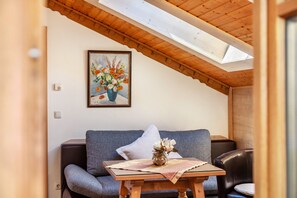 A cozy room with a wooden ceiling, a sofa, a table with a vase of flowers, and a painting on the wall. - Apartment 'Wohnung 4' with Mountain View, Balcony and Wi-Fi (Mittenwald)