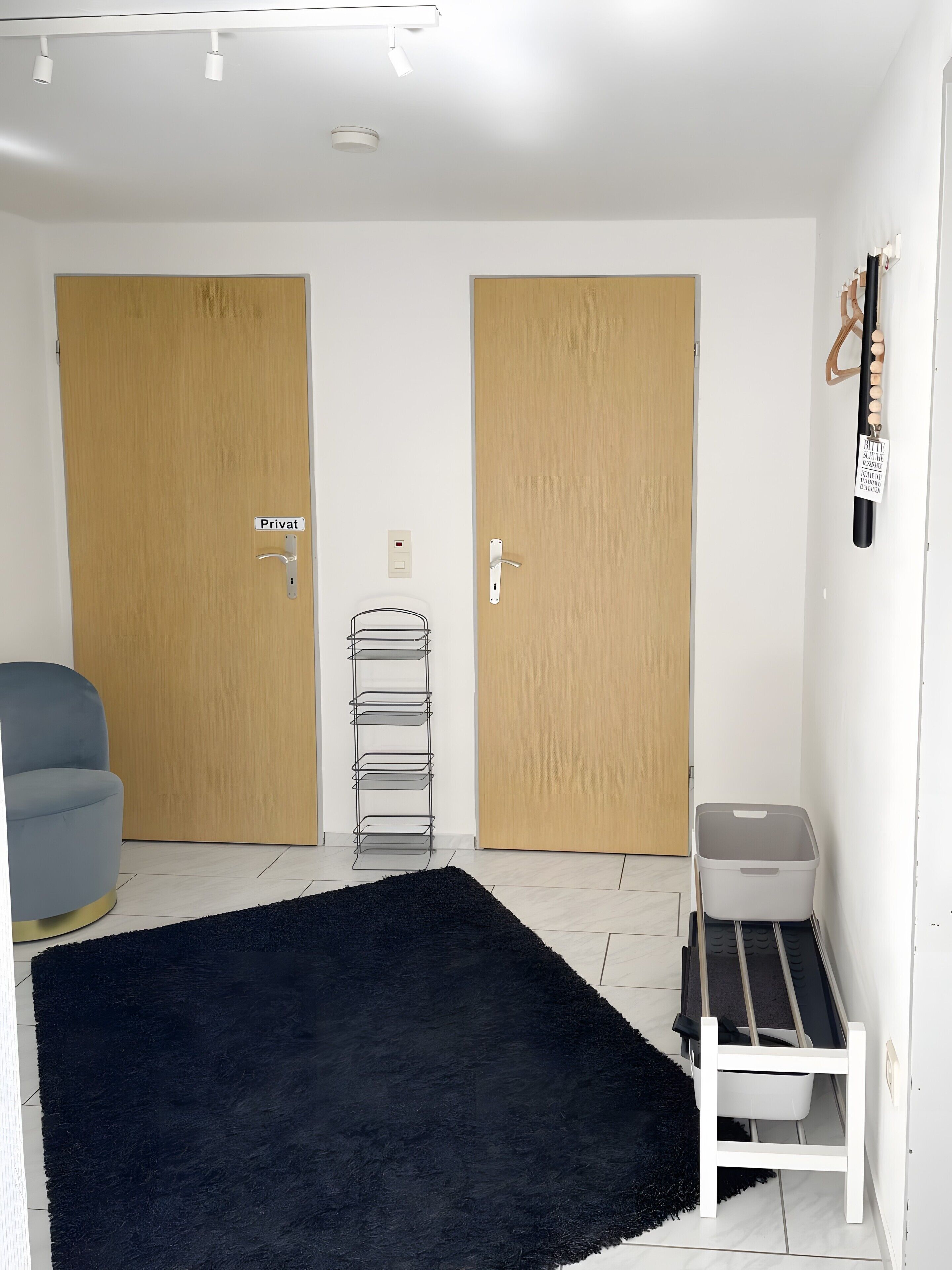 Habitació amb dues portes de fusta amb la inscripció ‘Privat’, una catifa negra i esponjosa, una panca grisa per emmagatzemar i un cub grís per a guardat.