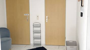 Habitació amb dues portes de fusta amb la inscripció ‘Privat’, una catifa negra i esponjosa, una panca grisa per emmagatzemar i un cub grís per a guardat.