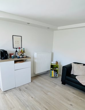 Un espace de vie moderne comprenant un coin cuisine, un radiateur, une bibliothèque et un canapé noir.