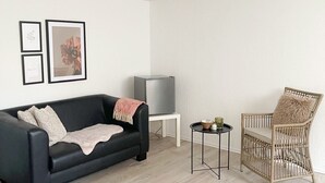 Ein modernes Wohnzimmer mit einem schwarzen Sofa, einem Korbstuhl, einem kleinen Beistelltisch und einem Fernseher.
