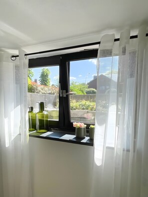 Quarto com janela, cortinas brancas e vista para o verde lá fora.