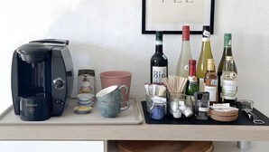 Eine Kaffeemaschine, ein gerahmter Spruch und verschiedene Flaschen und Tassen auf einem Tablett.