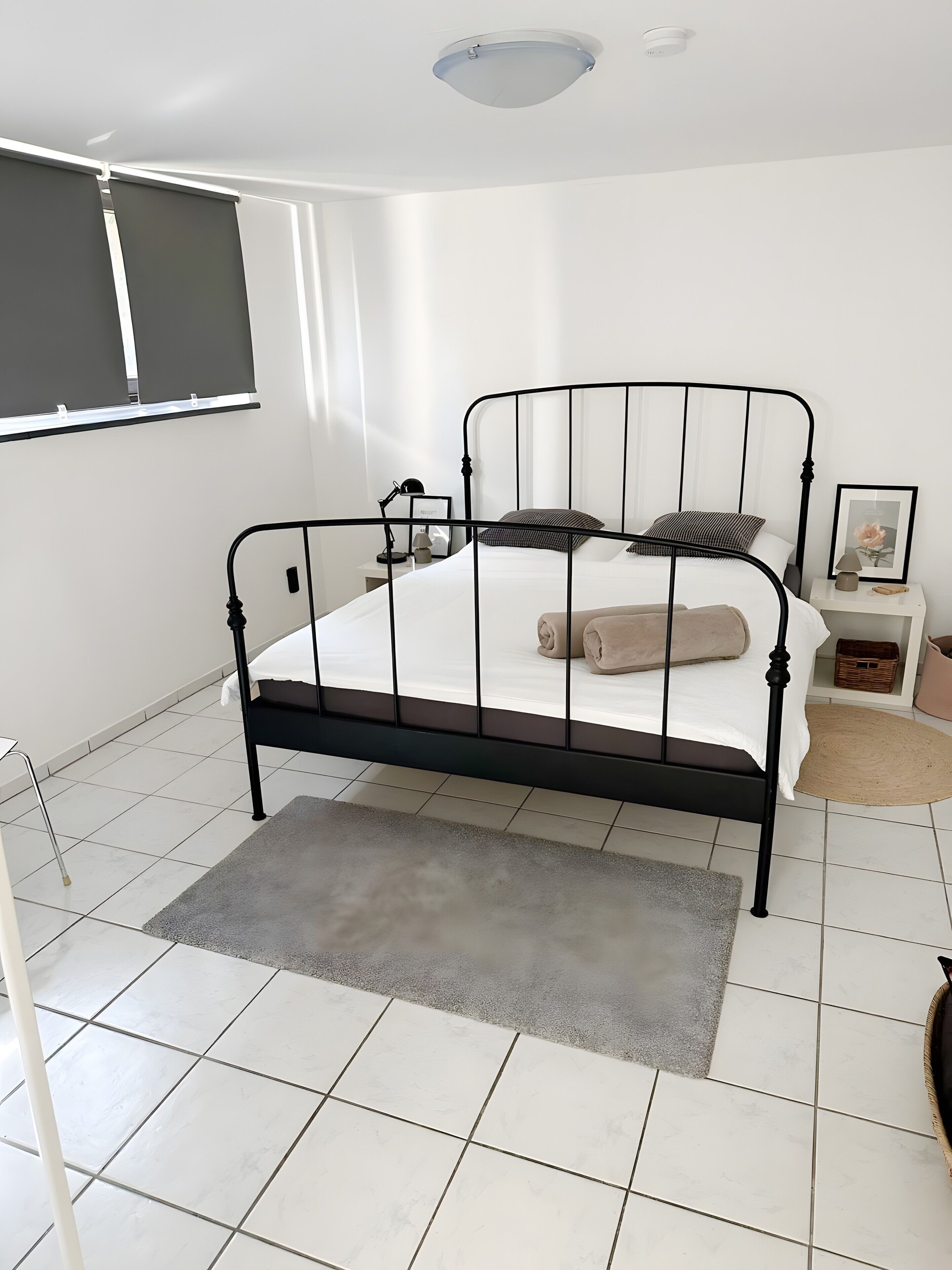 A bedroom with a metal bed frame, white bedding, a bedside table with a lamp, and a small picture frame.