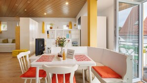 A modern interior with a dining area featuring a white table and chairs, a kitchen in the background, and a large sliding glass door to the right.