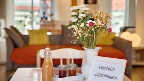 A table with a bottle, jars, a flower arrangement, and a welcome sign in a hotel room.