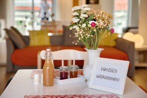 Une table avec une bouteille, des bocaux, un arrangement floral et un panneau d’accueil dans une chambre d’hôtel.