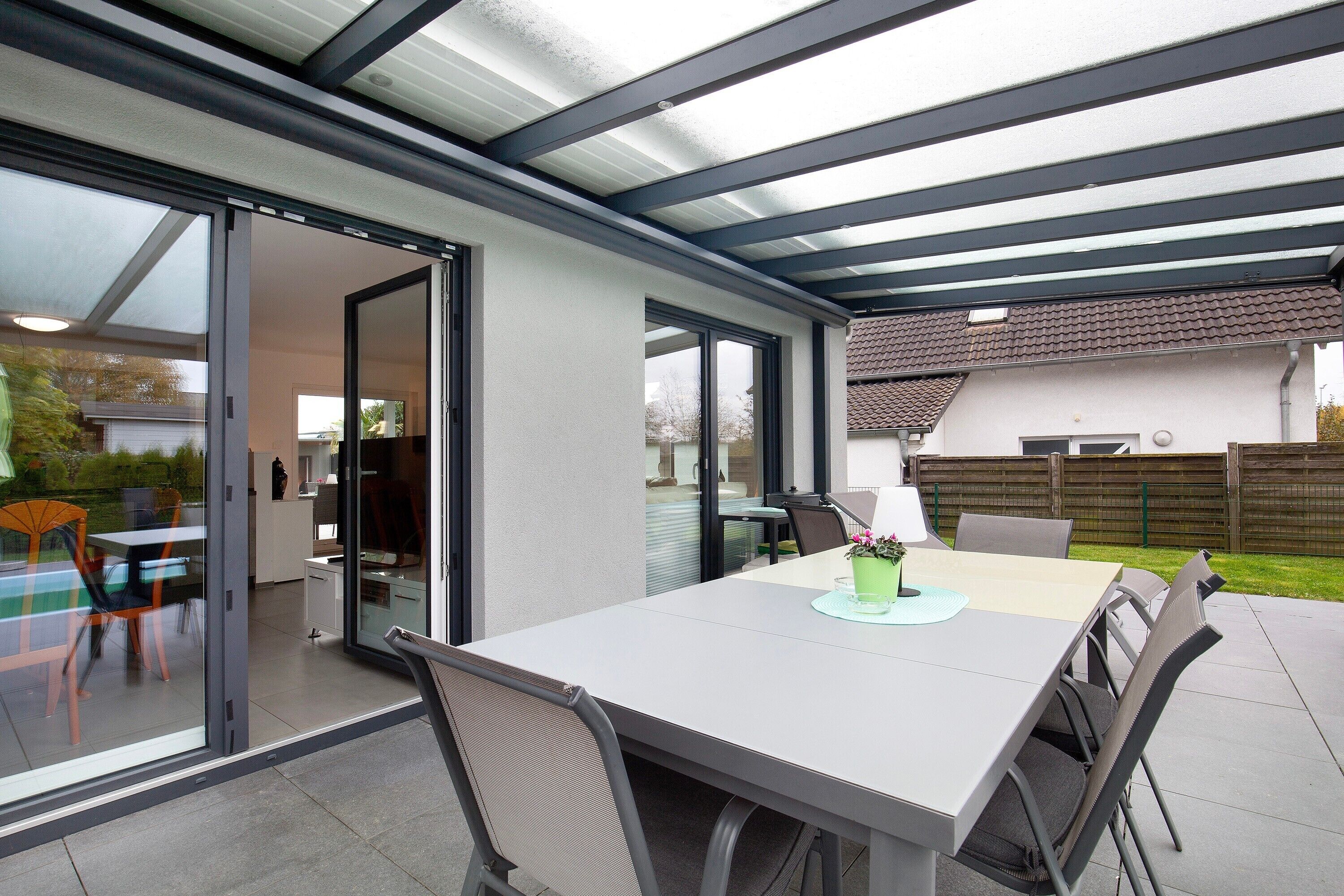 An outdoor patio with a table and chairs, a glass door leading to a kitchen, and a covered area with a roof.