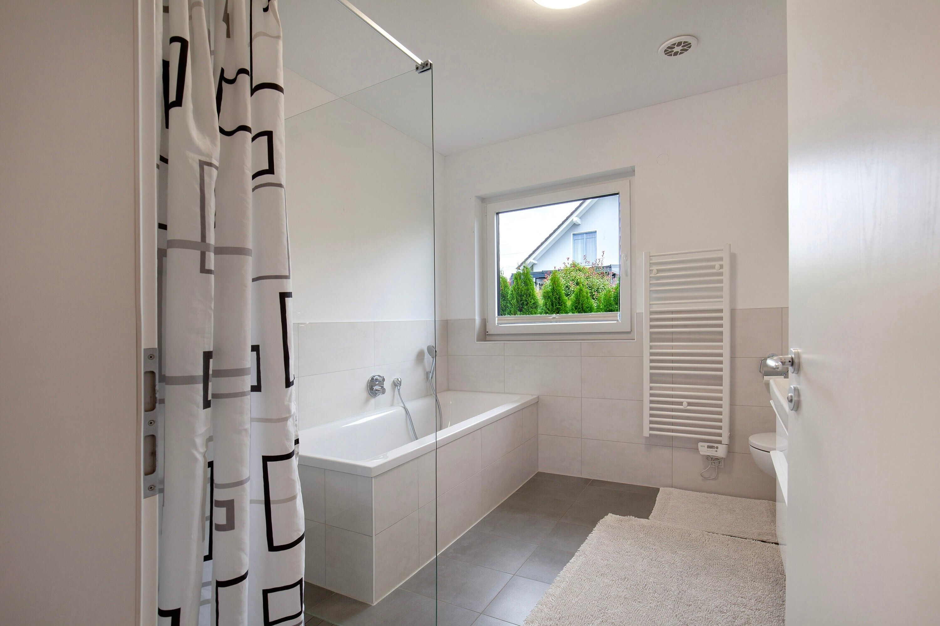 A modern bathroom with a bathtub, a window, and a radiator.