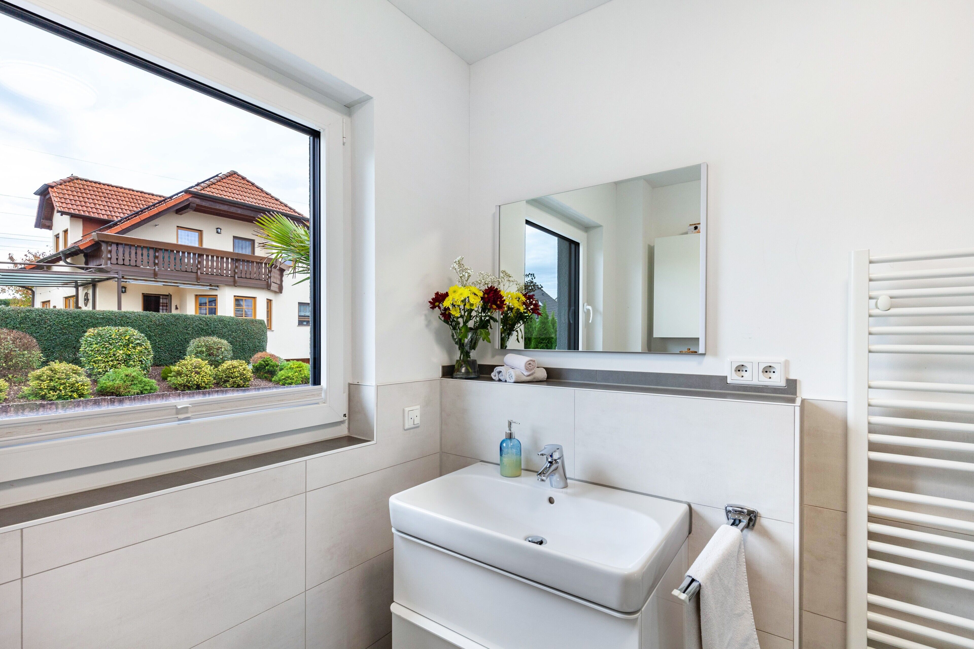 A modern bathroom with a window, a sink, a mirror, and a towel rack.