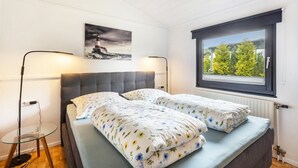 Een slaapkamer met een bed, twee bedlampen, een glazen tafel, een schilderij en een raam met uitzicht.