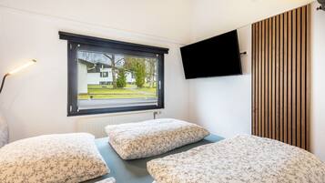 A bedroom with a bed, a window, a wall-mounted TV, and a radiator.
