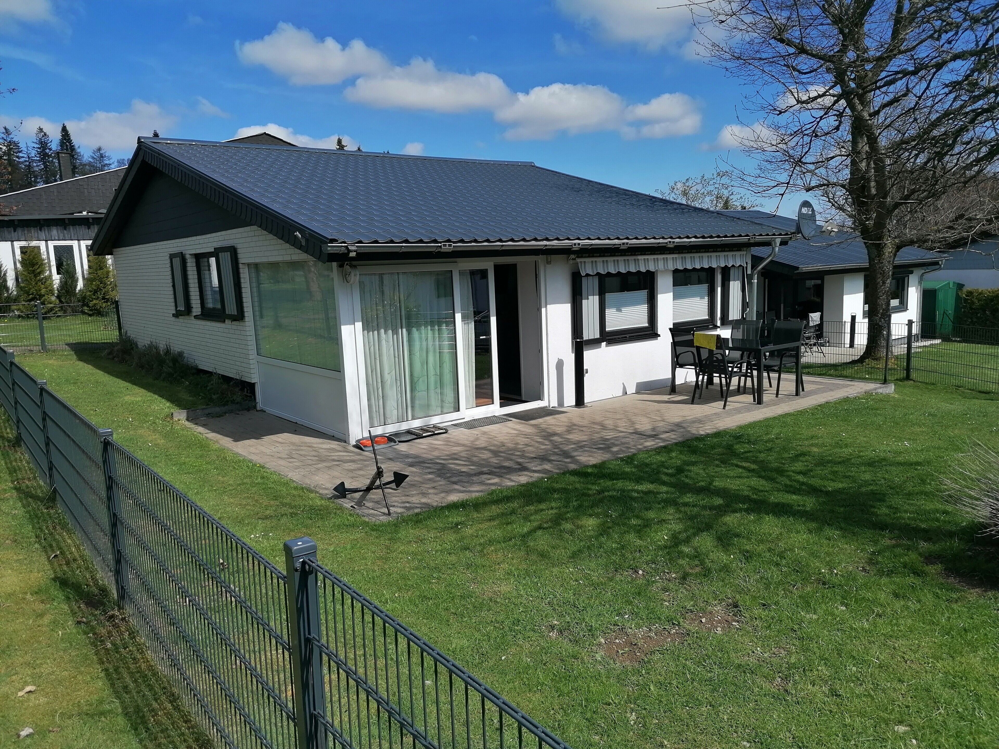 Een gelijkvloers huis met een overdekte veranda, een omheinde tuin en een schotelantenne.