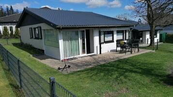 Een gelijkvloers huis met een overdekte veranda, een omheinde tuin en een schotelantenne.