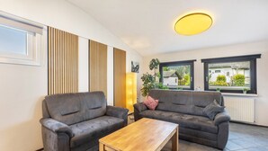 Een woonkamer met twee grijze banken, een houten salontafel, een hoge vloerlamp en uitzicht door grote ramen.
