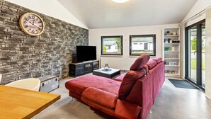 Ein modernes Wohnzimmer mit Steinwand, einem roten Sofa, einem Flachbildfernseher und einem Holzessttisch.