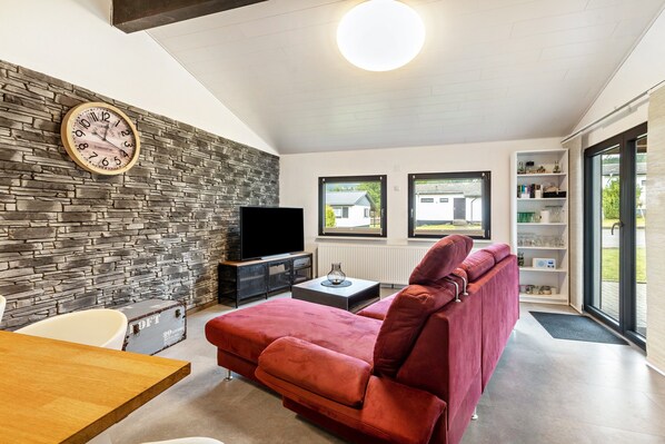 A modern living room with a stone wall, a red sofa, a flat-screen TV, and a wooden dining table.