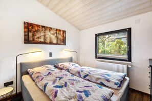 A bedroom with a bed, a window with a view, a painting on the wall, and a floor lamp.