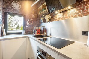 A modern kitchen with a brick wall, a window, a clock, a coffee maker, and a built-in oven.