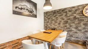 Ein Essbereich mit einem Holztisch, weißen Stühlen, einer Uhr und einer Wand mit Steinmuster.