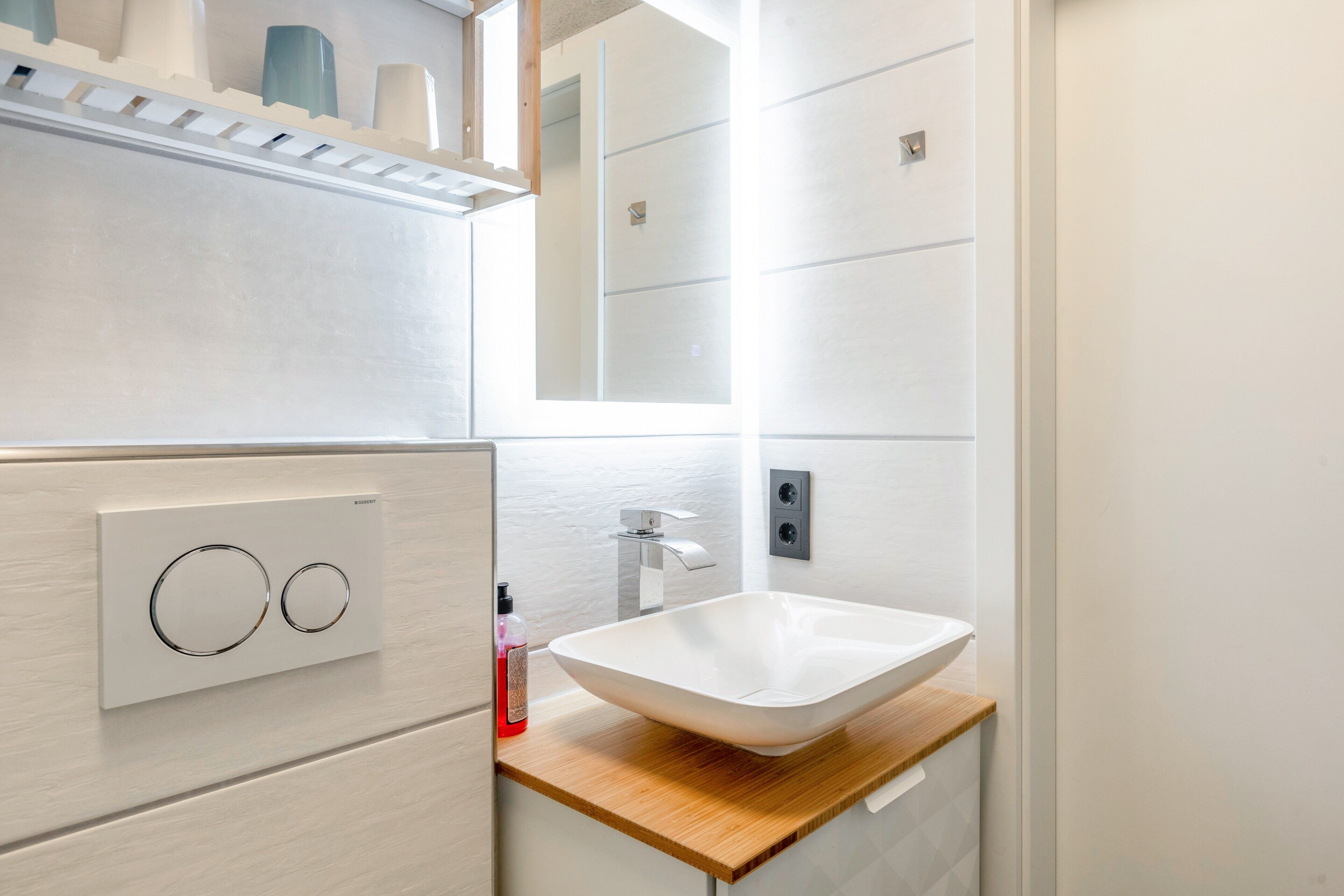 A modern bathroom with a white sink, wooden countertop, and a mirror above the sink.