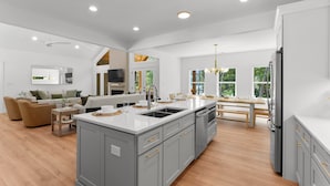 Une cuisine moderne avec des meubles gris, un îlot central et un coin repas comprenant une table et des chaises en bois.
