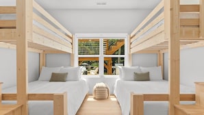 Une pièce avec deux lits superposés en bois, une fenêtre centrale et un petit pouf.
