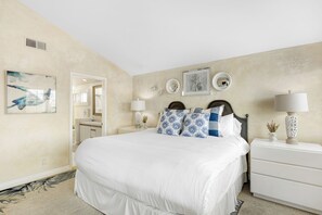 Une chambre à coucher avec un grand lit, deux tables de chevet, une commode et des œuvres d’art murales.