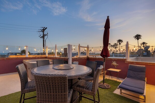 Une terrasse extérieure avec une table ronde, des chaises en osier, un parasol rouge et un fauteuil de relaxation.