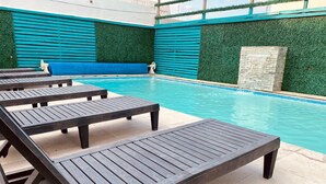 Una piscina con sillones de descanso y un muro de piedra.