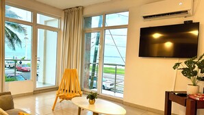 Una habitación con un ventanal grande, un televisor de pantalla plana, una mesita con una planta y una silla.