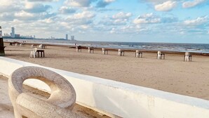 Una playa con una escultura de concreto, sillas blancas y una barandilla blanca.