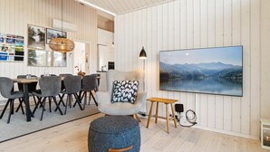 A modern living room with a large painting of a lake, a grey armchair, a round ottoman, and a dining area with grey chairs and a wooden table. - "Kristiarn" - 1.1km from the sea by Interhome (Aakirkeby)