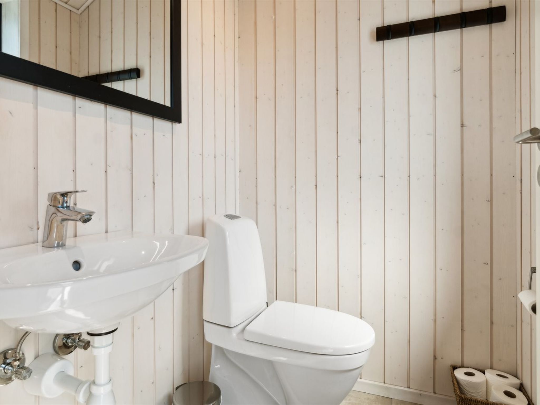 Et badeværelse med et hvidt håndvask, toilet og vægbeklædning af træ.