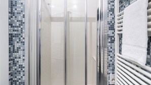 A glass-enclosed shower with a tiled mosaic wall and a white towel hanging on a rack.