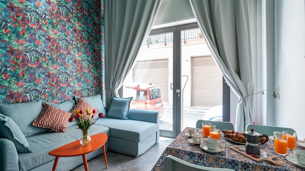 A modern living room with a sofa, a coffee table, and a breakfast table set with orange juice and pastries.