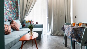 A living room with a sofa, a small table with a vase of flowers, and a dining area with a table set for breakfast.