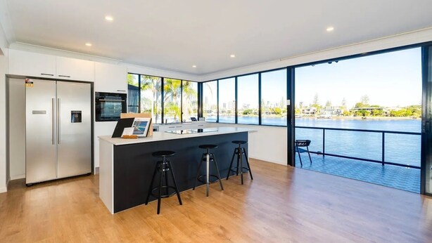 A modern kitchen with a large island, bar stools, and a view of a body of water.