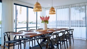 A modern dining area with a large table, black chairs, woven pendant lights, and a vase with flowers.