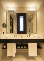 A modern bathroom with a large mirror, two sinks, and a shower.