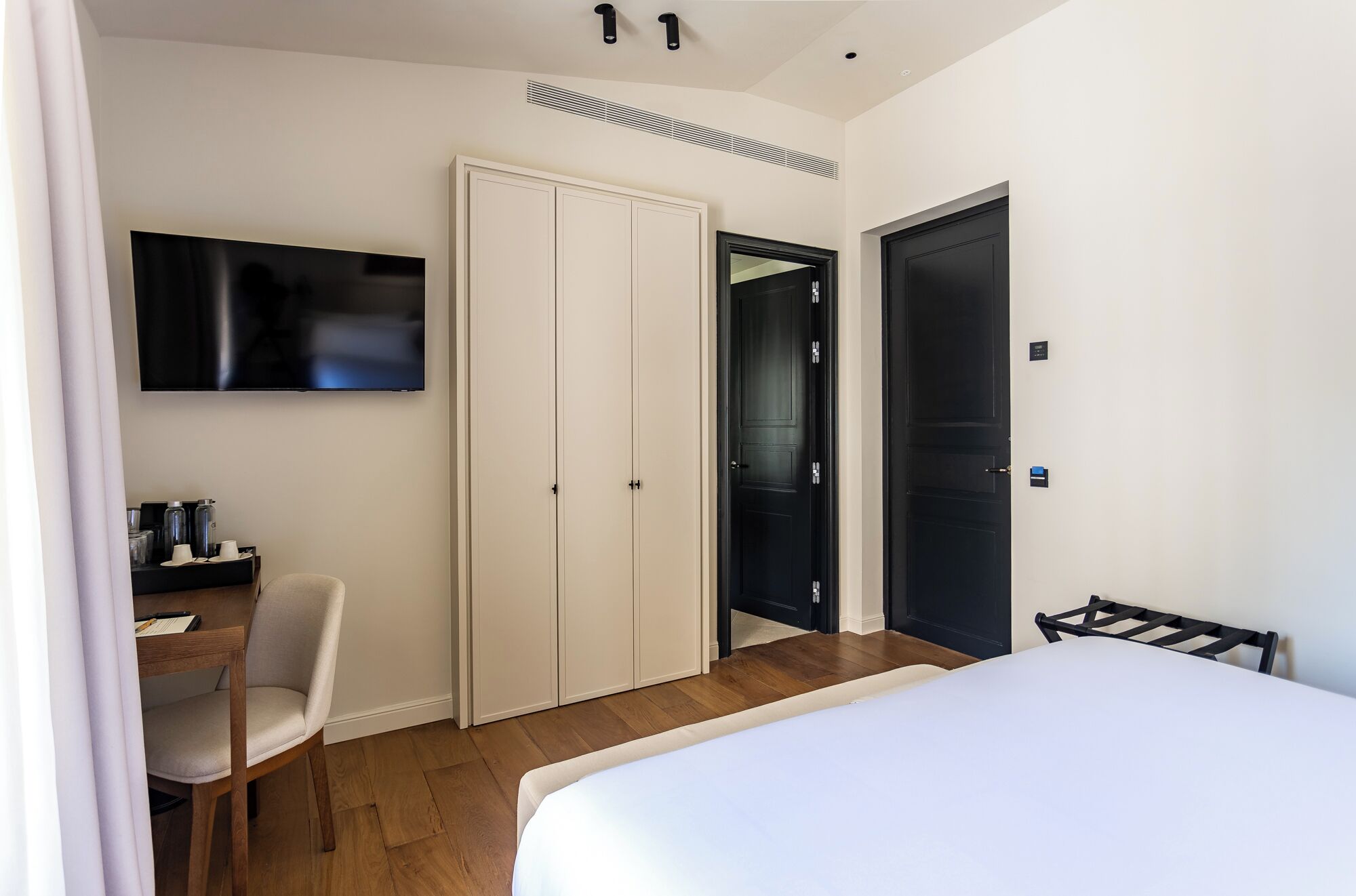 Ein Hotelzimmer mit einem Bett, einem Schreibtisch mit Stuhl, einem Fernseher und zwei Türen.