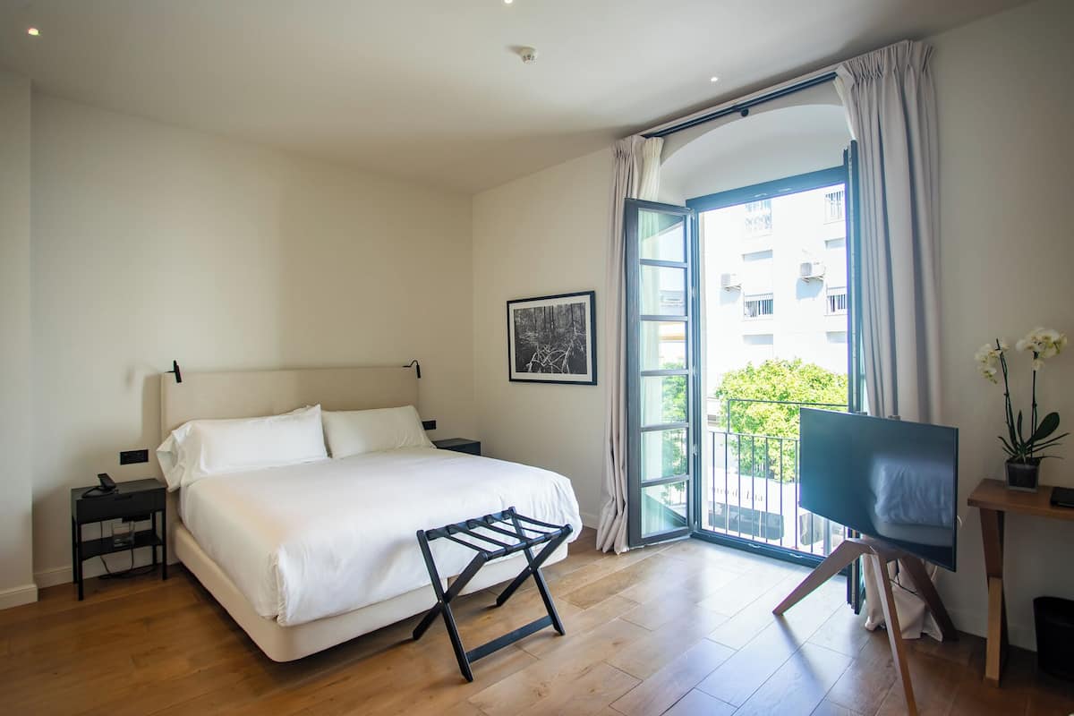 Un dormitorio con cama, escritorio, silla, ventana y balcón.
