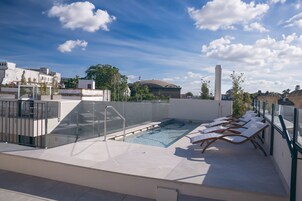 A rooftop pool area with lounge chairs and a glass barrier.