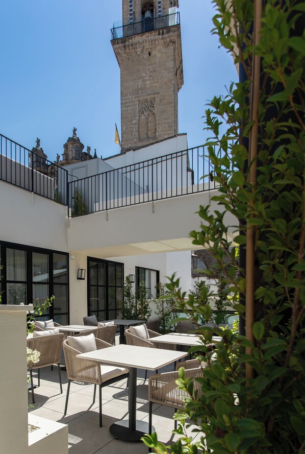 An outdoor patio area with tables and chairs, a stone tower, and a flag. - Hotel Boutique Sidonia (Jerez de la Frontera)