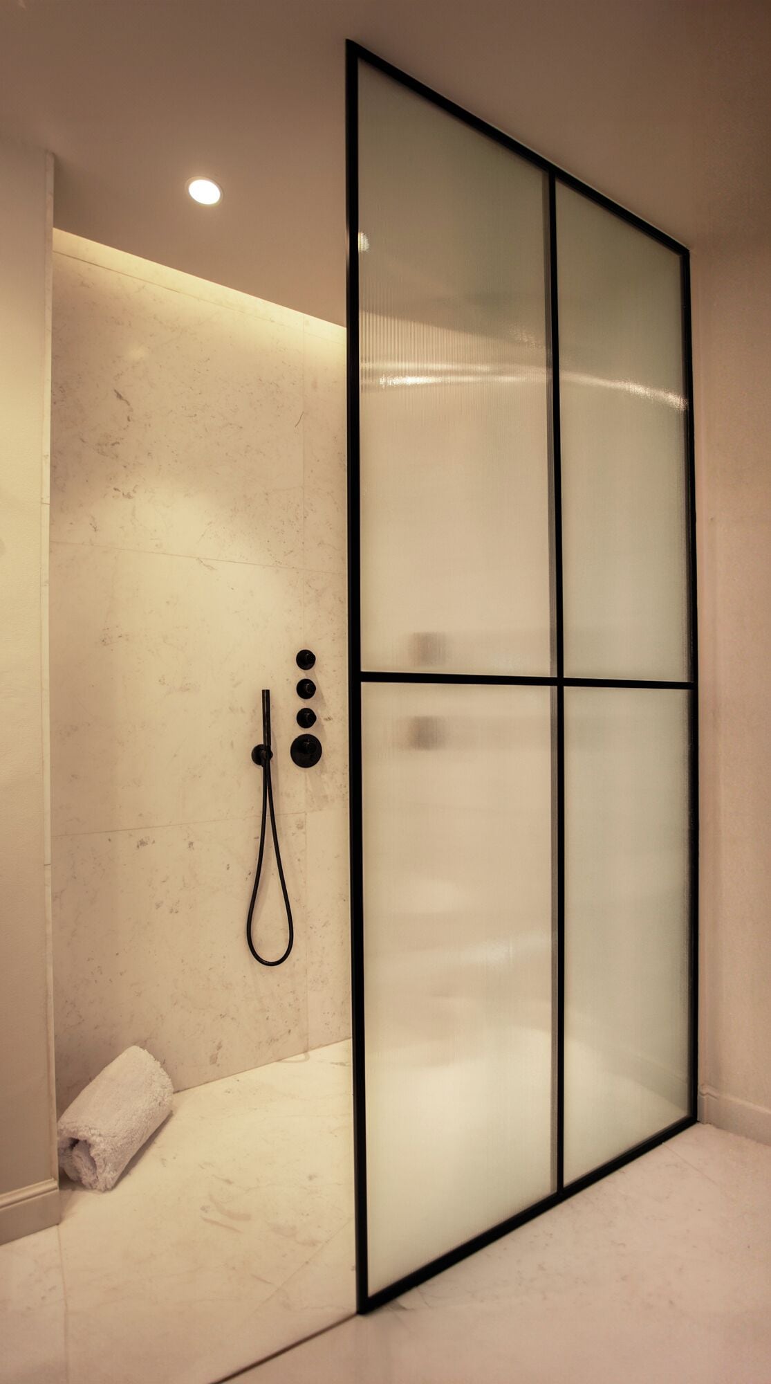 Un baño moderno con cabina de ducha de vidrio, ducha de mano y una toalla en el suelo.