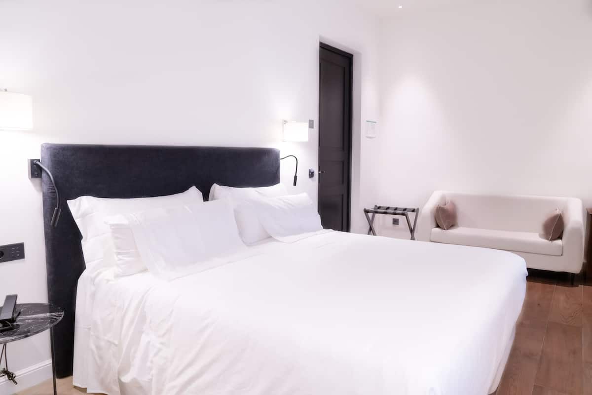 Una habitación de hotel moderna con una cama grande, un sofá blanco y una mesita pequeña.