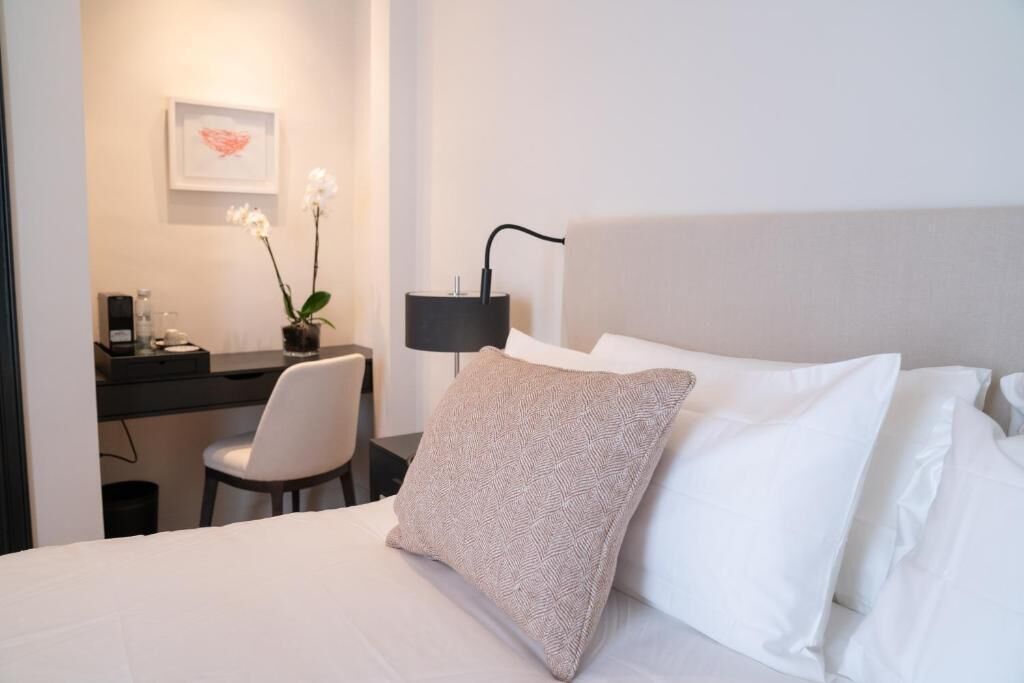 A hotel room with a bed, a desk, a chair, a lamp, and a framed picture on the wall.