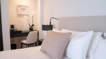 A hotel room with a bed, a desk, a chair, a lamp, and a framed picture on the wall.