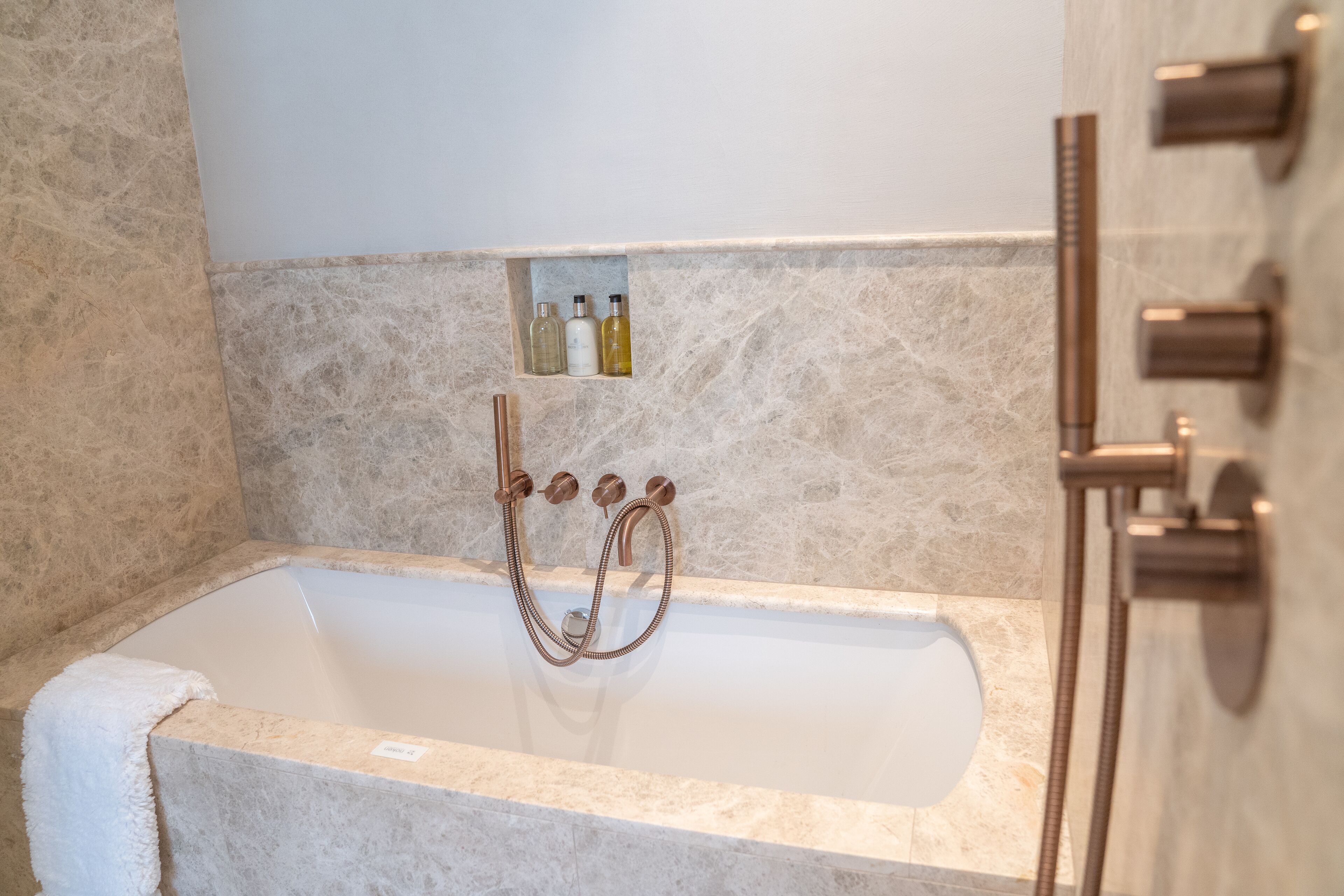 Un baño moderno con una bañera de mármol, un estante empotrado con artículos de aseo personal y una zona de ducha separada.