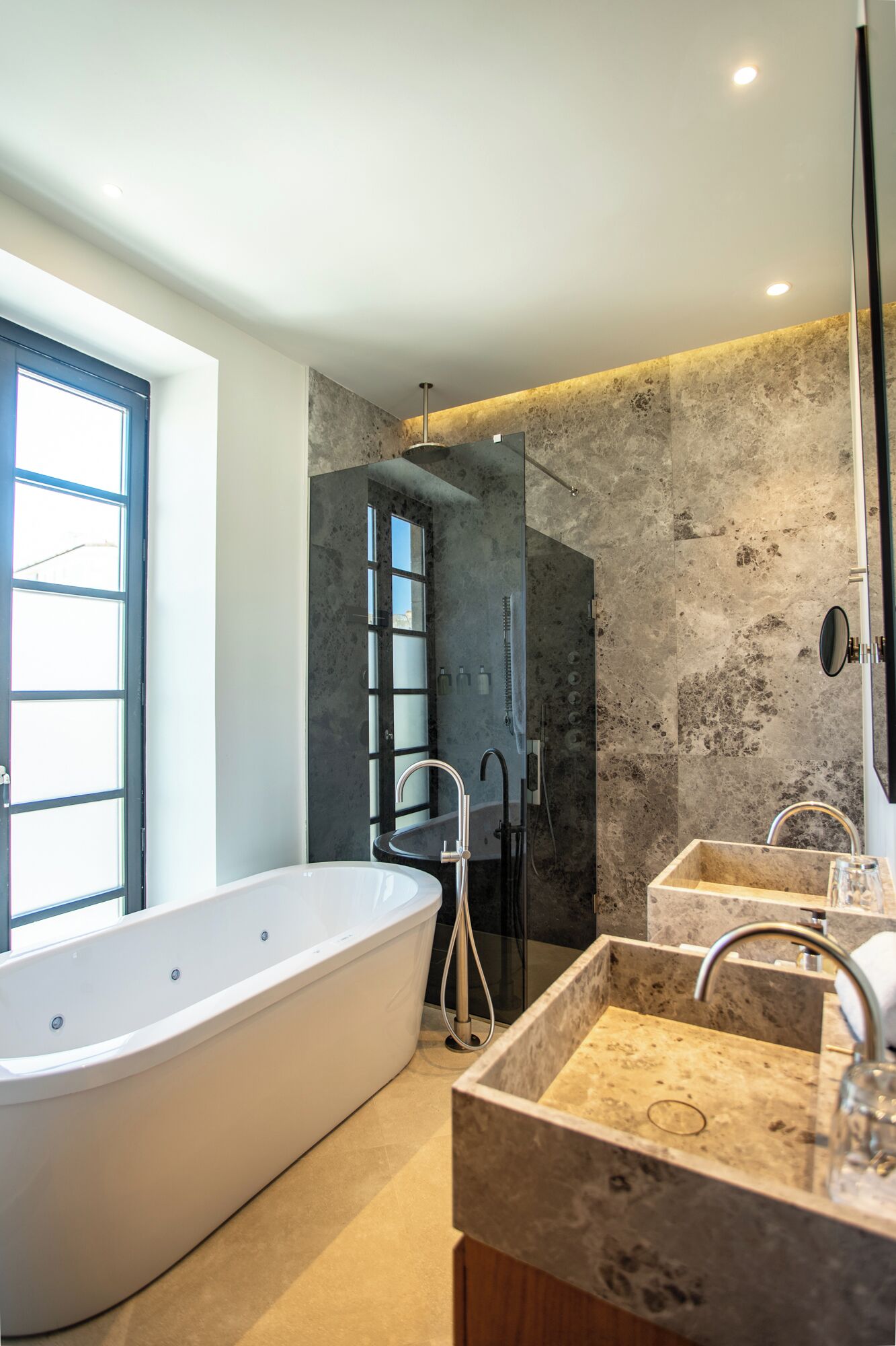 A modern bathroom with a freestanding bathtub, a walk-in shower, and two sinks.